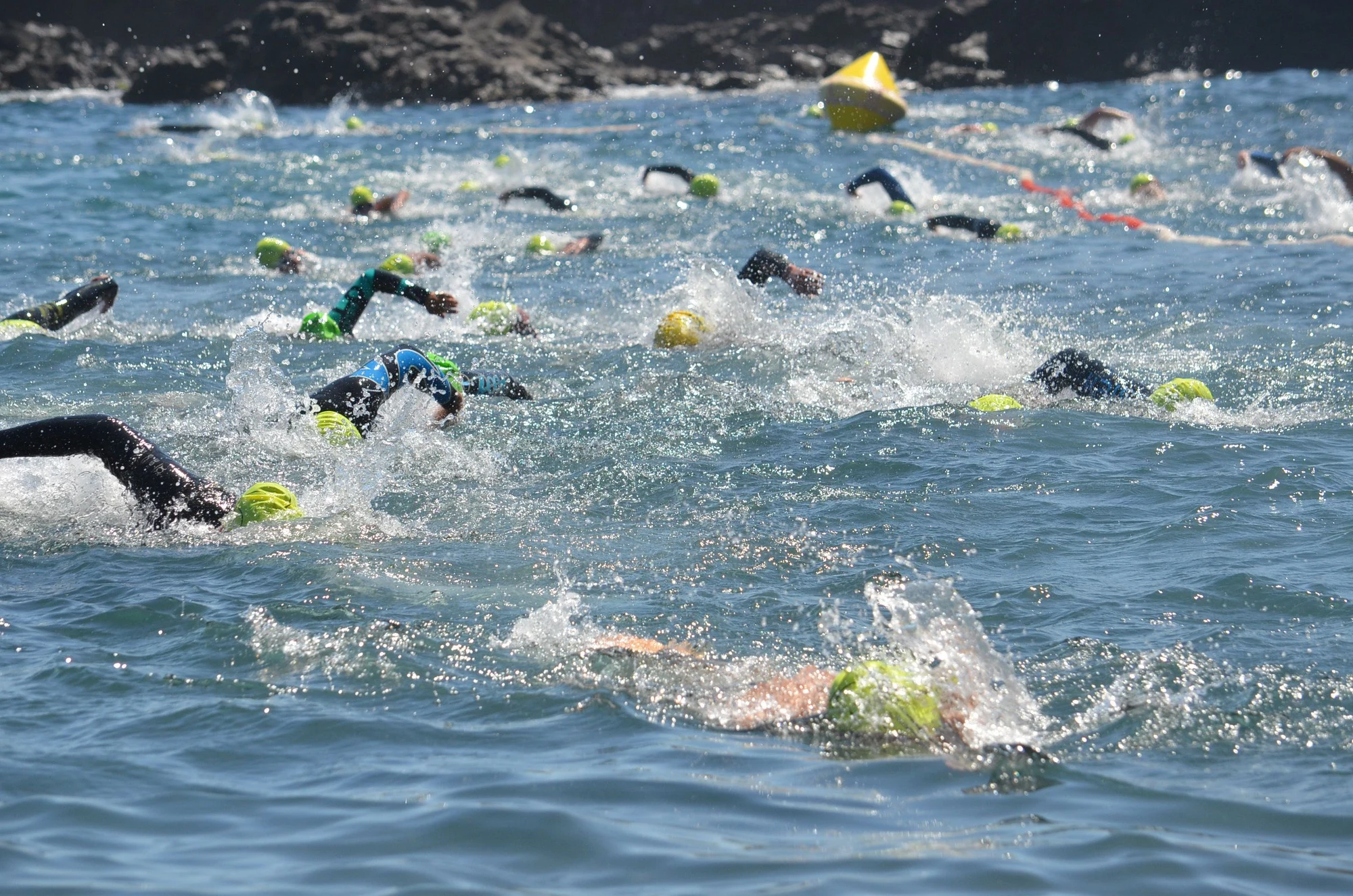 Open-water swimmers racing together towards a yellow buoy