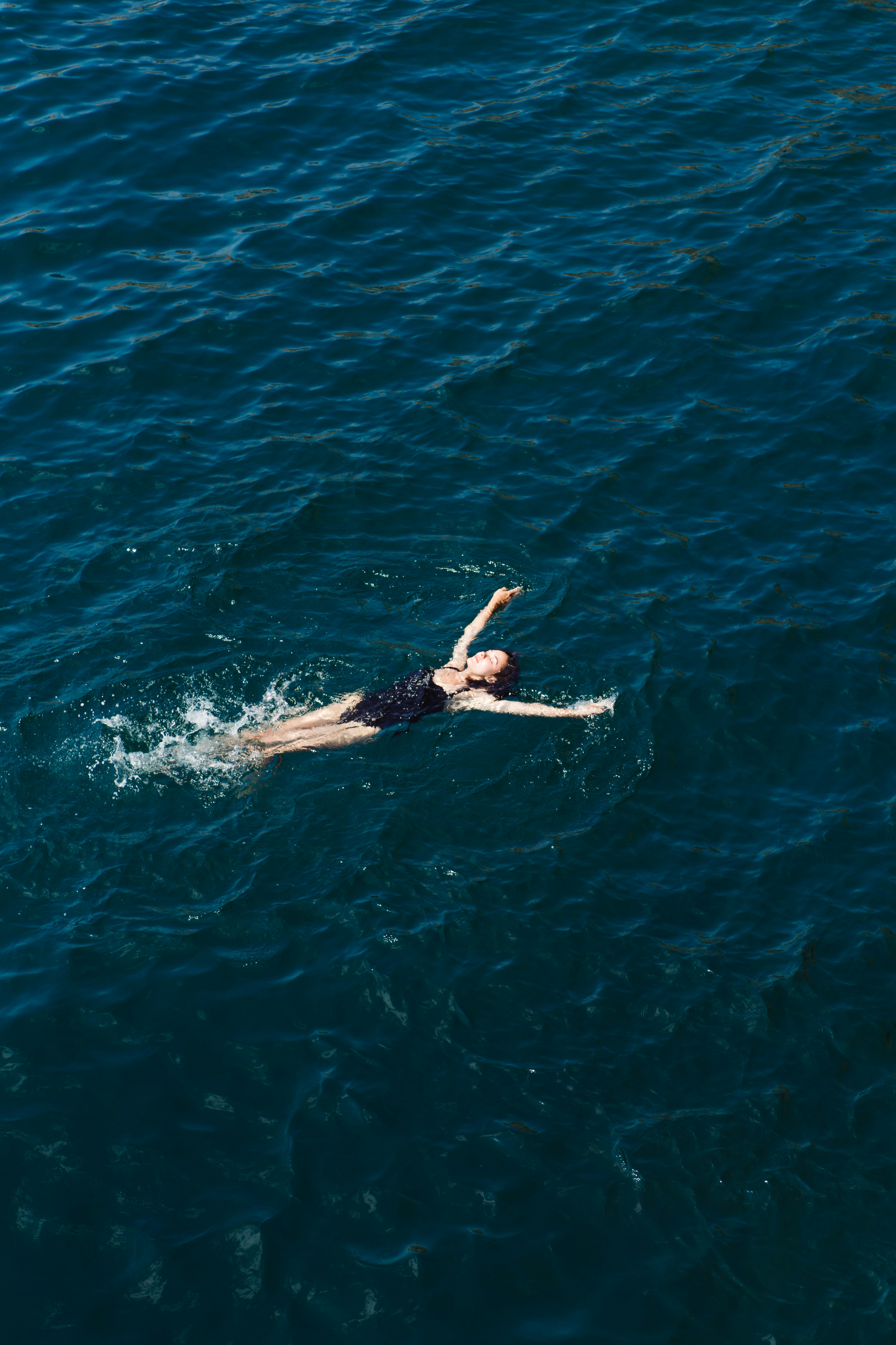 A swimmer floating on their back in deep blue open water, viewed from above